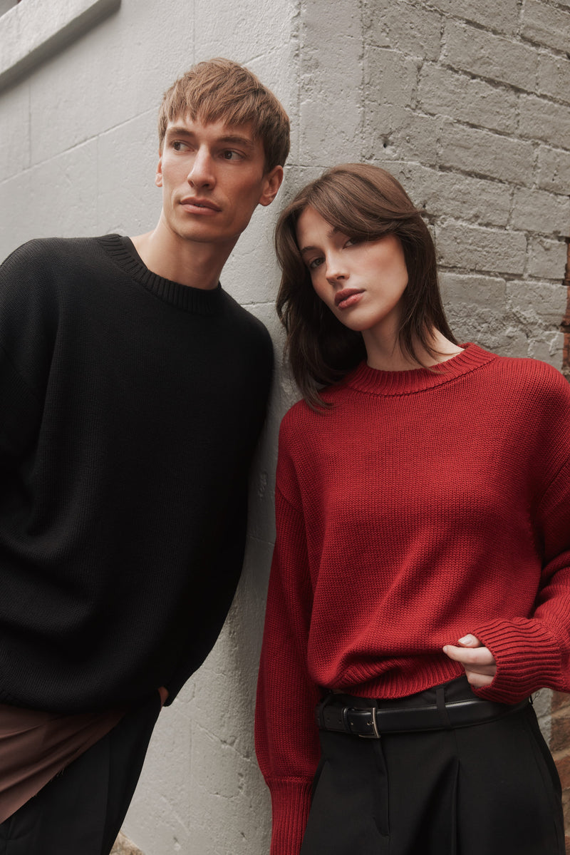 Two models in black and red SilKnit sweaters against a brick wall
