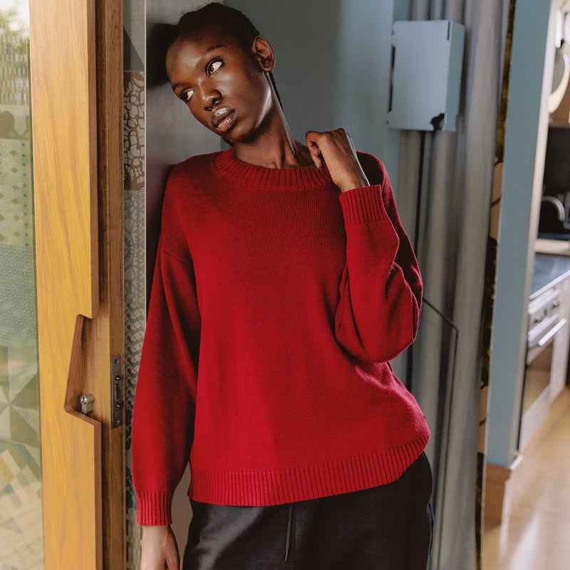 Model in a red SilKnit sweater in a warm interior